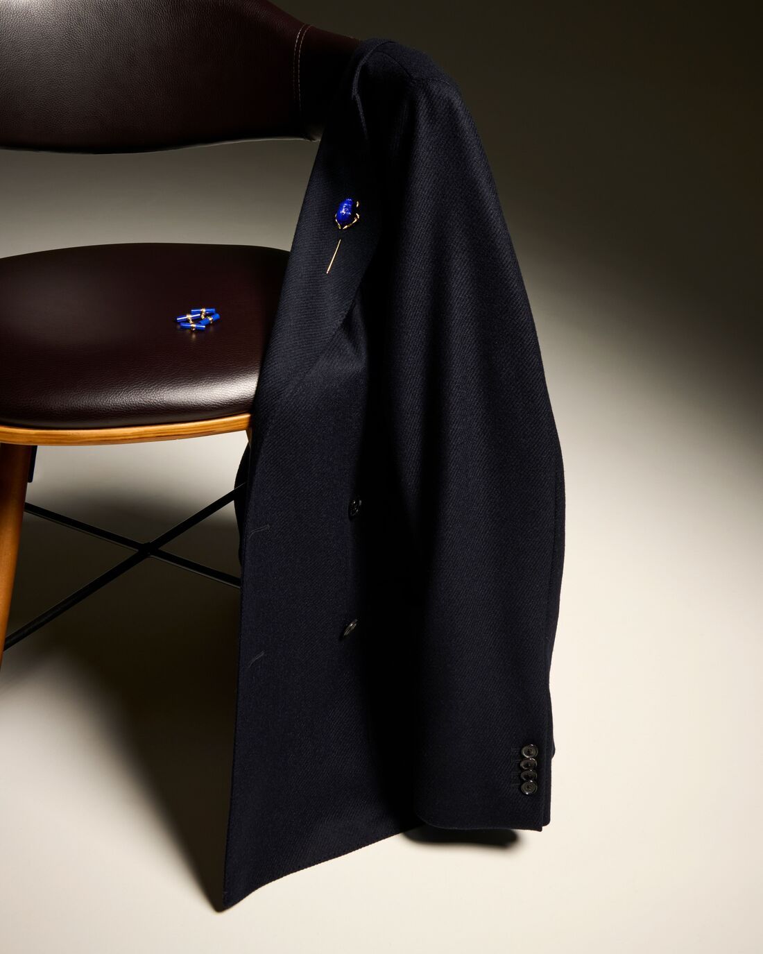 An elegant suit jacket with a lavish purple gemstone pinned to the lapel, is draped over the side of an antique chair